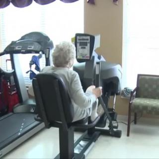 An elderly person exercising on gym equipment indoors.