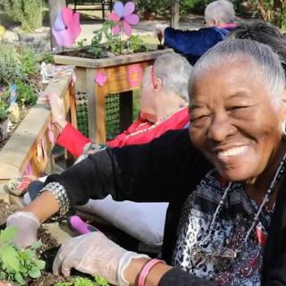 An elderly woman is joyfully gardening outdoors as part of a community activity.