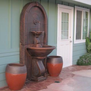An outdoor wall-mounted fountain accompanied by two large pots on a patio.