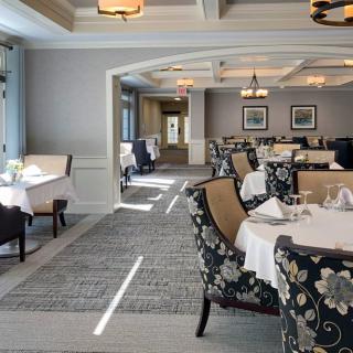 An elegantly decorated dining room with neatly arranged tables and chairs, featuring white tablecloths and floral-patterned upholstery.
