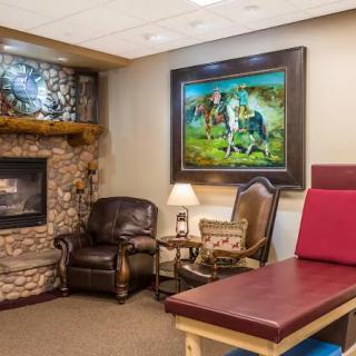 A cozy waiting room featuring a stone fireplace, leather armchairs, and a colorful painting on the wall.