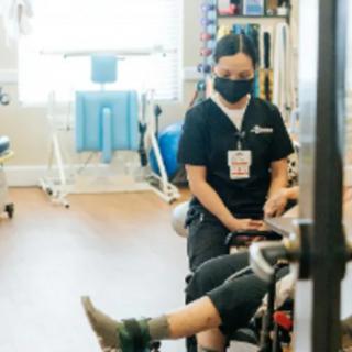 A healthcare professional assists a patient with physical therapy exercises in a rehabilitation setting.