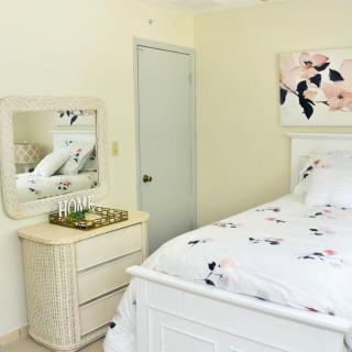 A cozy bedroom with a floral-themed decor, featuring a bed, dresser with mirror, and a wall painting.