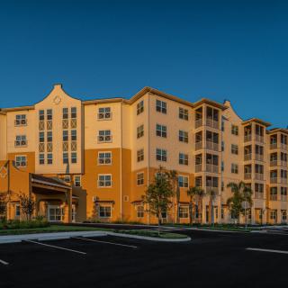 A modern multi-story apartment building with well-maintained landscaping, captured during the evening.