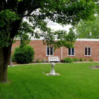 A brick building surrounded by a green lawn and trees, with a small fountain in the forefront.