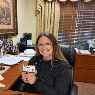 A woman smiling while holding a card at her office desk.