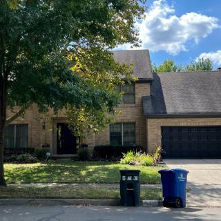 A suburban house with a driveway and trash cans at the curb.