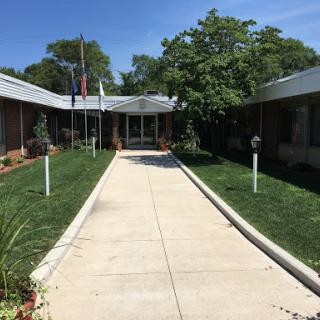 A serene pathway leads to a well-maintained building, surrounded by greenery and flags.