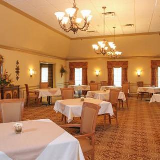 An elegant dining room with neatly arranged tables and chairs, illuminated by large chandeliers.