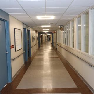 A quiet hallway inside a hospital, featuring doors on either side and well-lit pathways.