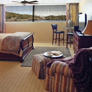 A cozy bedroom with a large bed, armchair, and a window offering a scenic view.