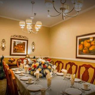 An elegantly set dining room with a large table, surrounded by chairs and adorned with a beautiful flower centerpiece. The room is illuminated by a chandelier and decorated with wall art.