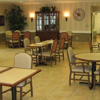 An empty dining area with several tables and chairs, featuring a wall clock and a wooden cabinet.