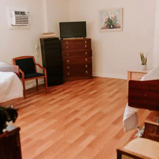A tidy bedroom with wooden floors, containing a bed, chairs, a dresser, and a TV.