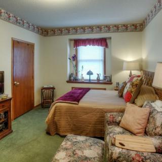 A cozy bedroom with a neatly made bed, patterned chair, and decorative elements on the window sill.