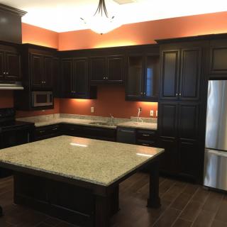 A modern kitchen with dark cabinets, a granite island, and stainless steel appliances.