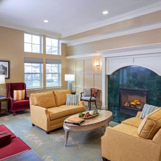 A cozy living room with beige sofas and a fireplace, featuring a modern coffee table and ample natural light from large windows.