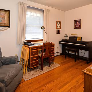 A cozy home office featuring a desk, chair, piano, and wall art.