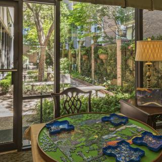 A cozy indoor space with a table set for a board game, overlooking a lush garden through large windows.