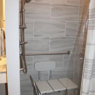 An accessible shower with grab bars and a shower chair, featuring a tiled wall.