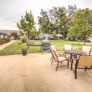 A spacious outdoor patio area with a table, chairs, and a grill surrounded by a lush garden.