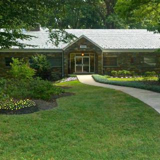 A small building surrounded by lush greenery and a well-maintained garden with a pathway leading to the entrance.