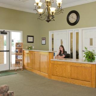 A welcoming reception area with a wooden desk, chandelier, and clock on the wall.