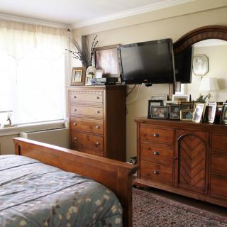 A cozy bedroom with wooden furniture, including a bed, dresser, and mirror, featuring a television mounted above the dresser.