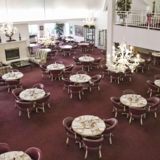 An elegant restaurant dining area with multiple round tables and chairs, adorned with chandeliers and a carpeted floor.