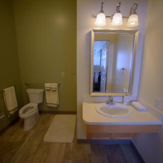 A modern bathroom with a sink, mirror, and toilet, featuring stylish lighting and tile flooring.