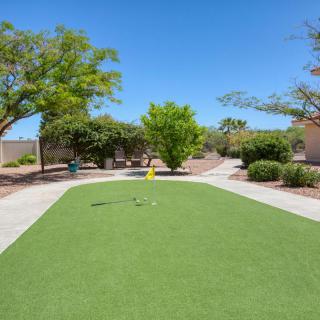 An outdoor mini golf putting green surrounded by trees on a sunny day.