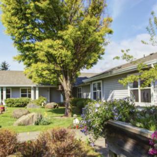 A charming residential house surrounded by a lush garden and trees on a sunny day.