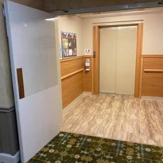 A well-lit hallway with an elevator and a partially open door, featuring wood paneling and carpeted flooring.