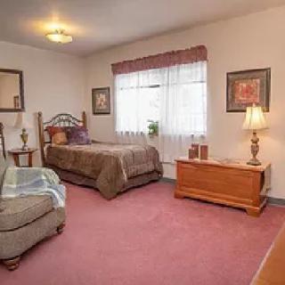 A cozy bedroom with a single bed and armchair, featuring warm decor and natural light from the window.
