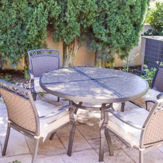 A cozy outdoor patio setup with a round table and four chairs surrounded by lush greenery.