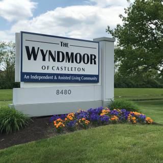 Sign for The Wyndmoor of Castleton, an independent and assisted living community, surrounded by a garden with flowers.