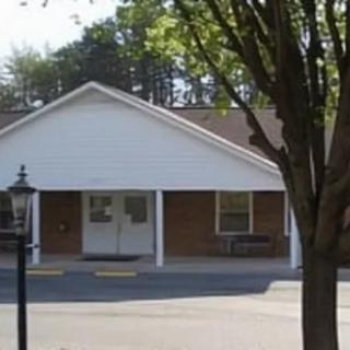 A small residential building with a covered entrance and surrounding trees.