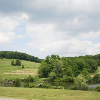 A serene landscape showcasing lush green hills and a calm body of water under a partly cloudy sky.