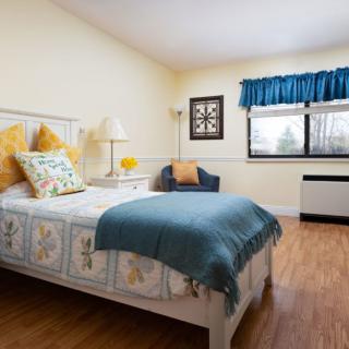 A cozy bedroom with a well-decorated bed, featuring colorful pillows and a blue throw blanket.