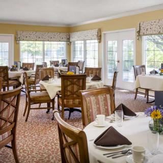 A well-lit dining room with elegantly set tables and large windows.