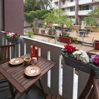 A cozy balcony setup with wooden furniture and decorative flowers overlooking a garden area.