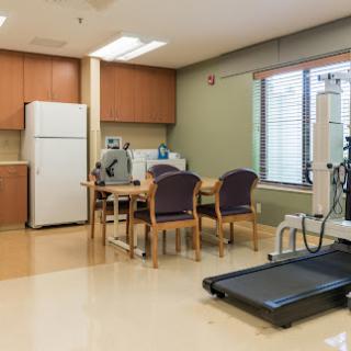 A clean and organized medical clinic space featuring a dining table, chairs, and rehabilitation equipment.