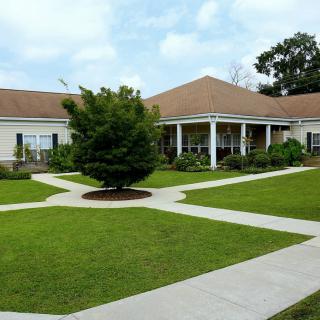 A building with a well-manicured lawn, intersecting pathways, and surrounding trees under a partly cloudy sky.