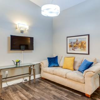 A cozy and modern living room with a beige sofa, colorful cushions, and a wall-mounted TV.