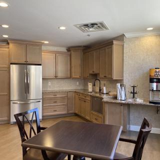 A modern kitchen interior featuring wooden cabinets, a dining table with chairs, a refrigerator, and a coffee machine.