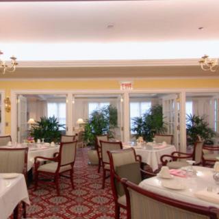 An elegantly decorated restaurant dining area with neatly arranged tables and chairs, complemented by indoor plants and a carpeted floor.