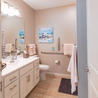 A modern bathroom with neutral tones and tasteful decor, featuring a sink, toilet, and wall art.