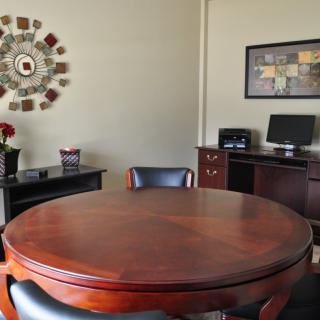 A well-appointed office space with a round wooden table, chairs, a computer, and decorative artwork on the walls.