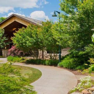 A serene garden pathway winding past lush greenery and trees towards a rustic building.
