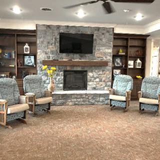A cozy living room with four armchairs arranged around a stone fireplace and a television, flanked by dark wooden bookshelves.